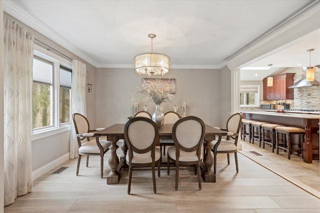 dining area featuring visible vents, a chandelier, crown molding, light wood finished floors, and baseboards