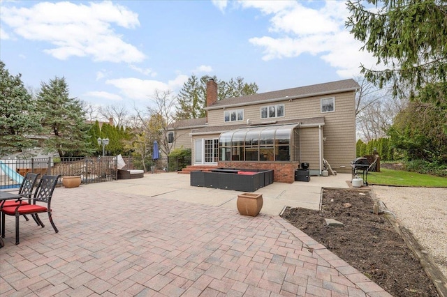 rear view of house featuring fence, a chimney, a sunroom, and a patio area