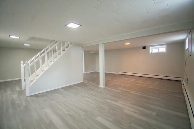 below grade area featuring wood finished floors, a baseboard heating unit, baseboards, and stairway