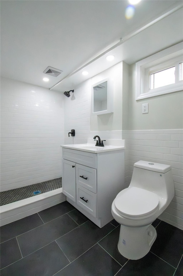 full bath with a tile shower, toilet, vanity, and tile walls
