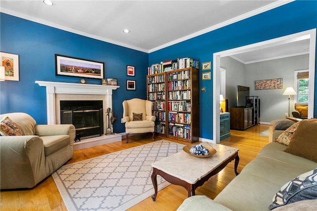 living area with crown molding, wood finished floors, a glass covered fireplace, baseboards, and recessed lighting