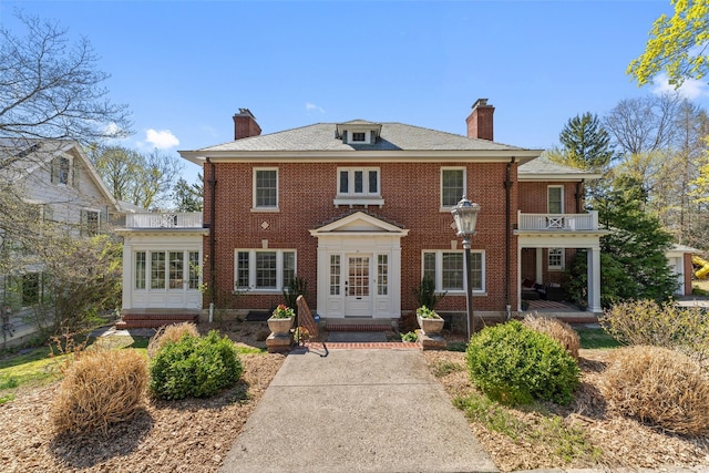 view of front facade with brick siding, a chimney, and a balcony