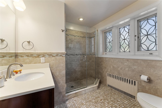 bathroom featuring vanity, toilet, radiator, tile walls, and a shower stall
