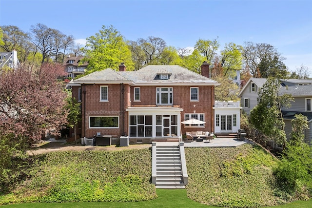 back of property featuring outdoor lounge area, a chimney, a sunroom, brick siding, and a patio area
