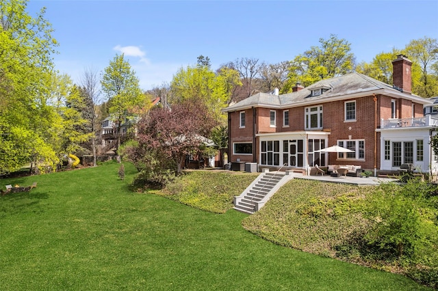 back of property featuring stairway, brick siding, a yard, and a chimney