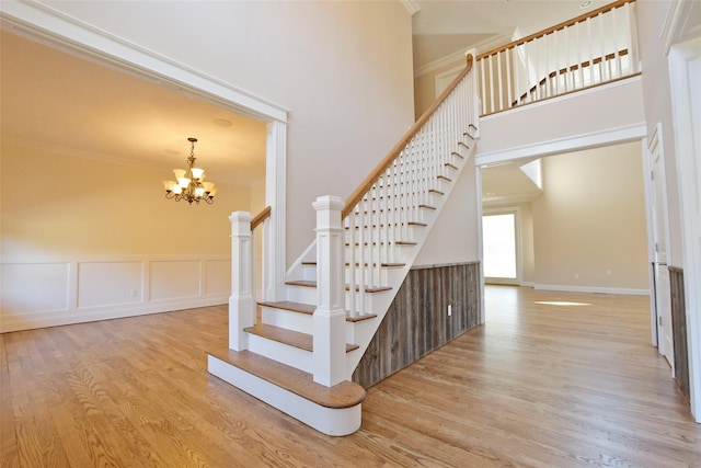 103 Silver Beech Ln, Calverton, NY 11933 - stairway featuring a wainscoted wall, crown molding, a chandelier, a high ceiling, and wood finished floors