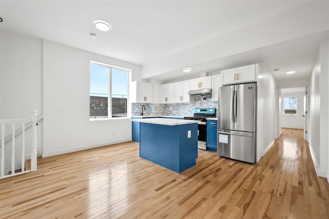 kitchen with white cabinets, under cabinet range hood, stainless steel appliances, light countertops, and a center island