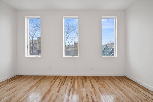 empty room featuring wood-type flooring, plenty of natural light, and baseboards