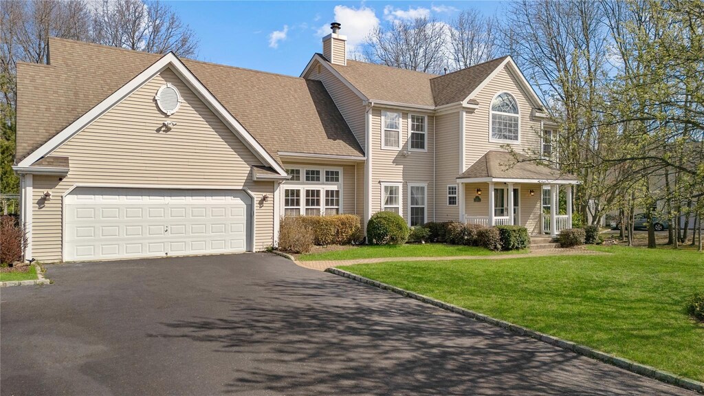 23 Varsity Blvd, East Setauket, NY 11733 - traditional-style house featuring a front yard, an attached garage, a chimney, driveway, and roof with shingles
