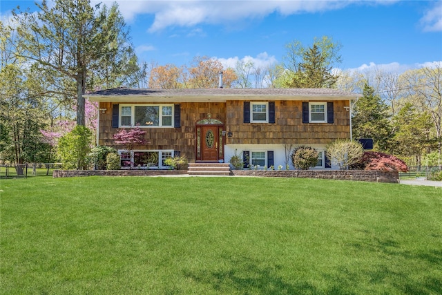 bi-level home featuring a shingled roof, fence, and a front yard