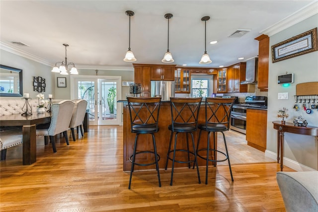 kitchen featuring brown cabinetry, appliances with stainless steel finishes, visible vents, and wall chimney range hood