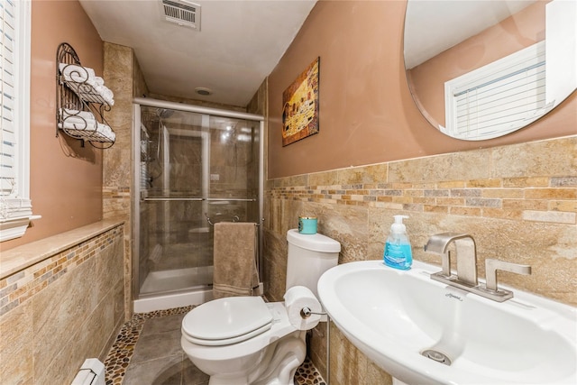 full bath with visible vents, a sink, tile walls, and a shower stall
