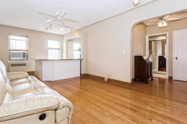 living room featuring light wood-style flooring, arched walkways, ceiling fan, and radiator heating unit