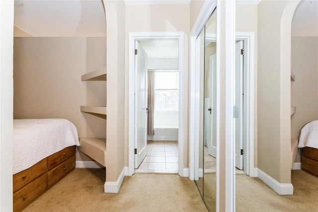 bedroom featuring arched walkways, connected bathroom, baseboards, and light carpet