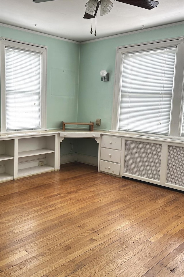 unfurnished office featuring ornamental molding, radiator, ceiling fan, and wood finished floors