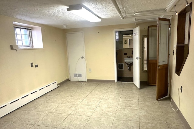 spare room featuring a textured ceiling, baseboard heating, light tile patterned floors, baseboards, and visible vents