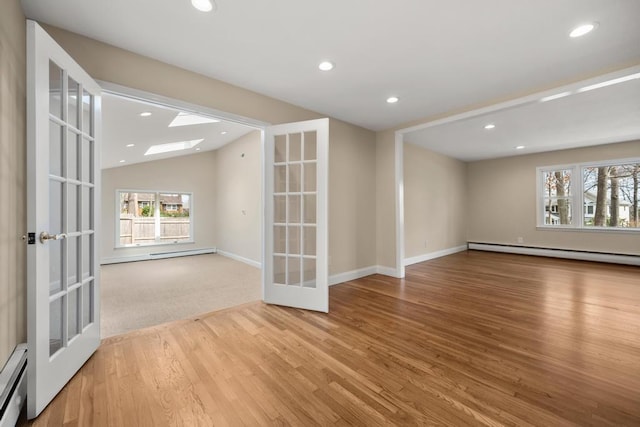 empty room with french doors, a baseboard heating unit, a healthy amount of sunlight, and wood finished floors