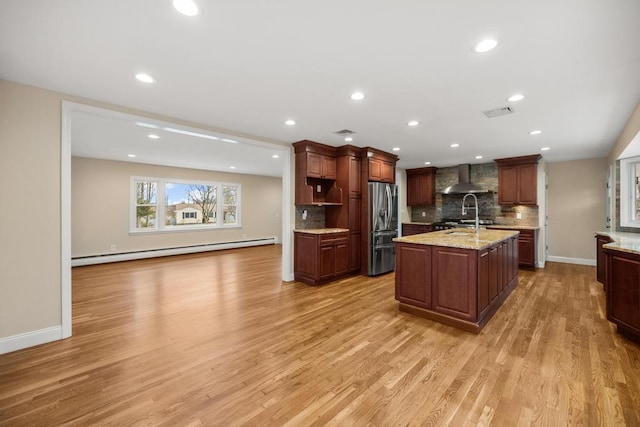 kitchen with stainless steel fridge, wall chimney exhaust hood, a baseboard radiator, light wood-style flooring, and backsplash