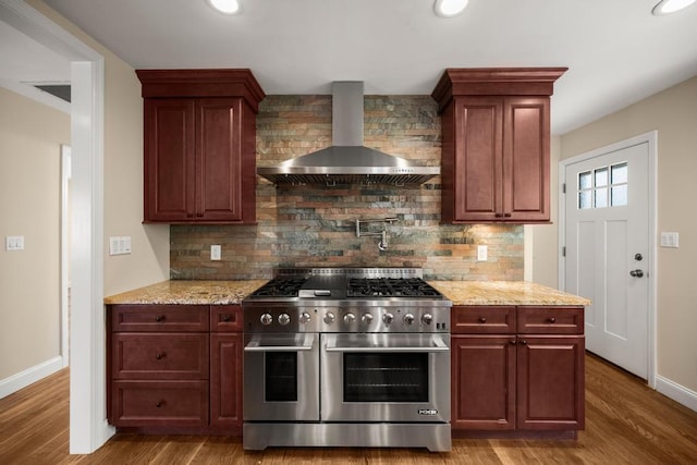kitchen with baseboards, decorative backsplash, wall chimney exhaust hood, and double oven range
