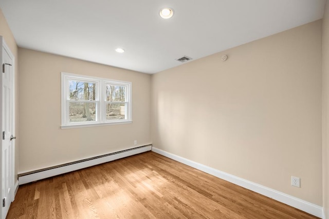 spare room featuring baseboards, baseboard heating, light wood-style flooring, and visible vents