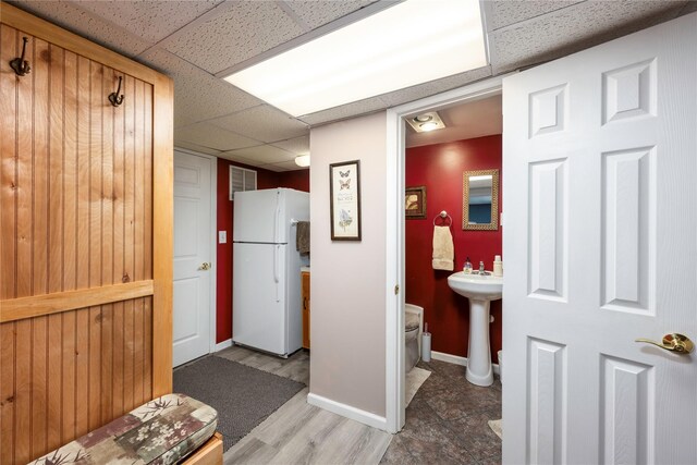 hallway featuring baseboards, a drop ceiling, and wood finished floors