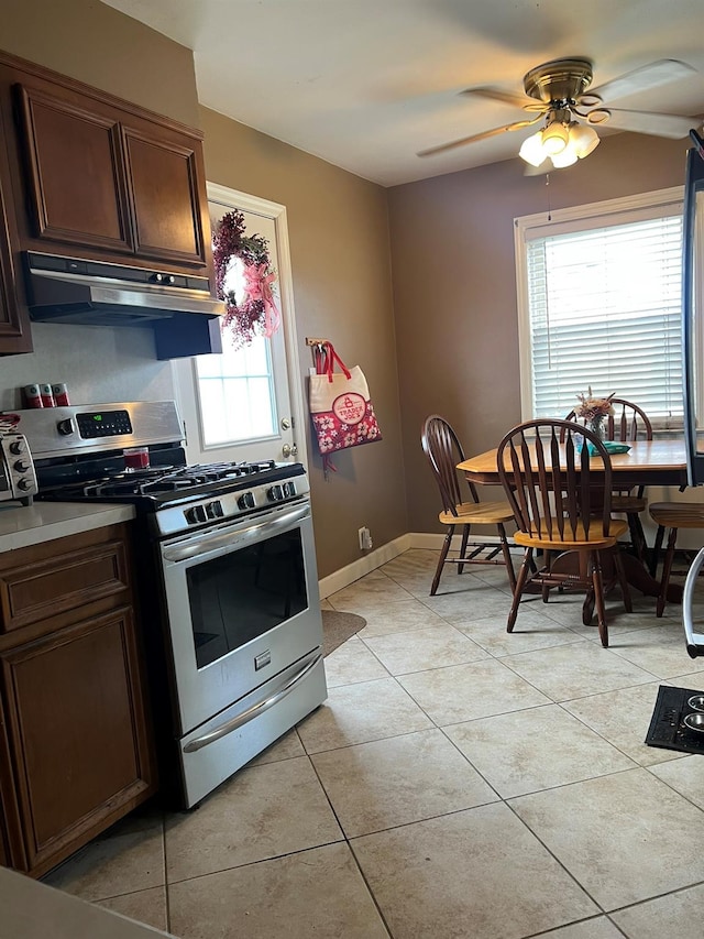 kitchen featuring stainless steel range with gas cooktop, dark brown cabinets, a ceiling fan, under cabinet range hood, and light tile patterned floors