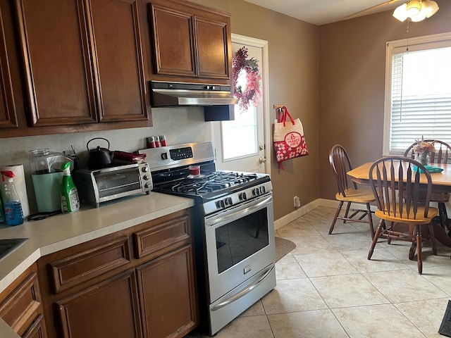 kitchen with a toaster, under cabinet range hood, light countertops, light tile patterned floors, and gas range