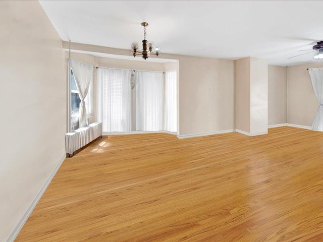 unfurnished room with baseboards, radiator heating unit, ceiling fan with notable chandelier, and light wood-style floors