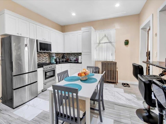 kitchen with radiator heating unit, recessed lighting, white cabinets, appliances with stainless steel finishes, and backsplash