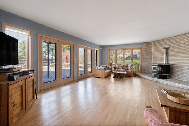 living area featuring light wood-style floors, a wood stove, french doors, and a wealth of natural light