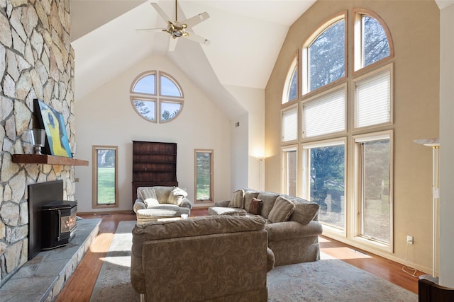 living area featuring high vaulted ceiling, ceiling fan, wood finished floors, and a wood stove