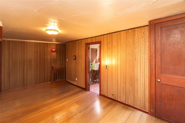 empty room featuring light wood finished floors, baseboards, and wood walls