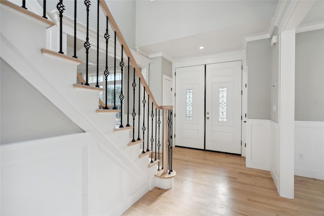 foyer with light wood-type flooring, ornamental molding, stairway, and a towering ceiling