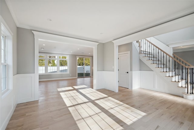 unfurnished living room featuring stairs, wainscoting, light wood-style flooring, and a decorative wall