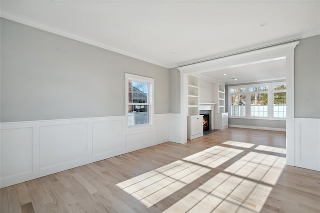 unfurnished living room featuring a healthy amount of sunlight, light wood-type flooring, and wainscoting
