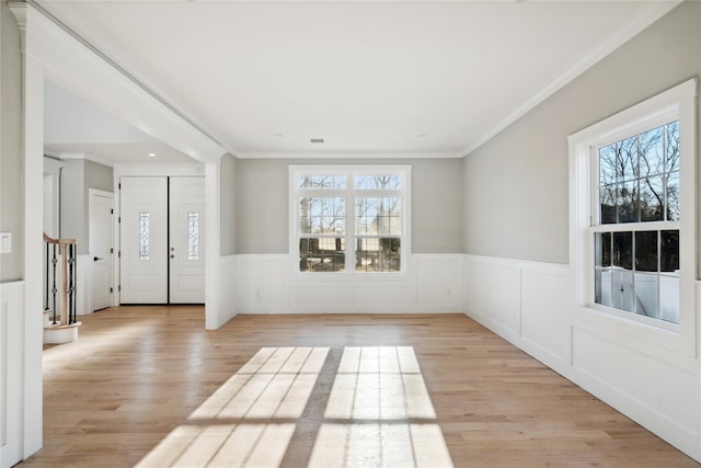 foyer entrance with ornamental molding, wainscoting, and a wealth of natural light