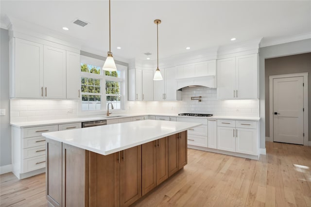kitchen featuring light countertops, light wood-type flooring, backsplash, a sink, and visible vents