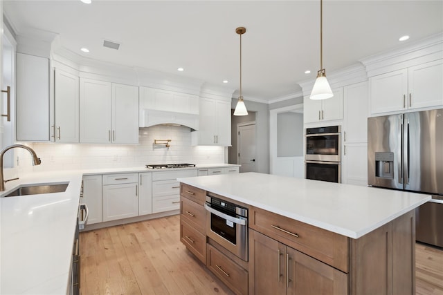 kitchen featuring crown molding, light wood finished floors, a sink, and appliances with stainless steel finishes