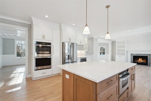 kitchen featuring light wood-style floors, appliances with stainless steel finishes, white cabinetry, a center island, and crown molding