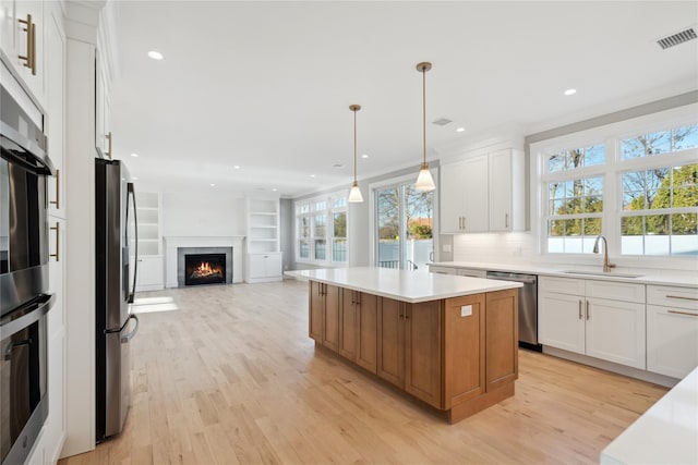 kitchen featuring light wood-style floors, appliances with stainless steel finishes, white cabinets, a sink, and a center island
