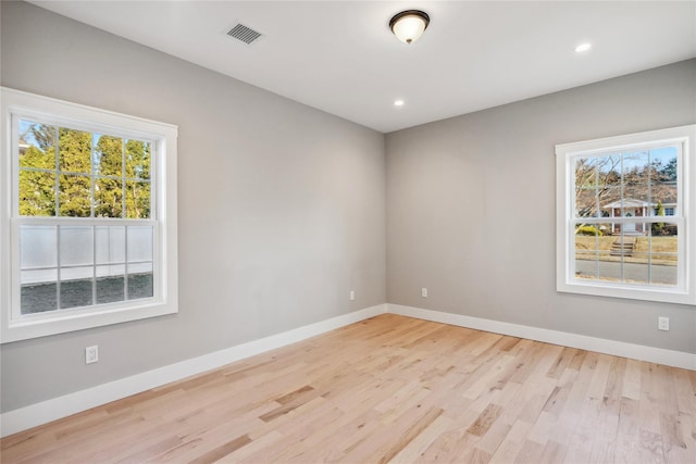 empty room featuring baseboards, visible vents, light wood-type flooring, and plenty of natural light