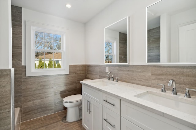 bathroom featuring double vanity, a sink, toilet, and tile walls