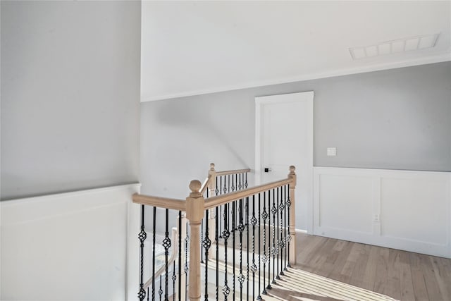 stairway with a decorative wall, a wainscoted wall, visible vents, and wood finished floors