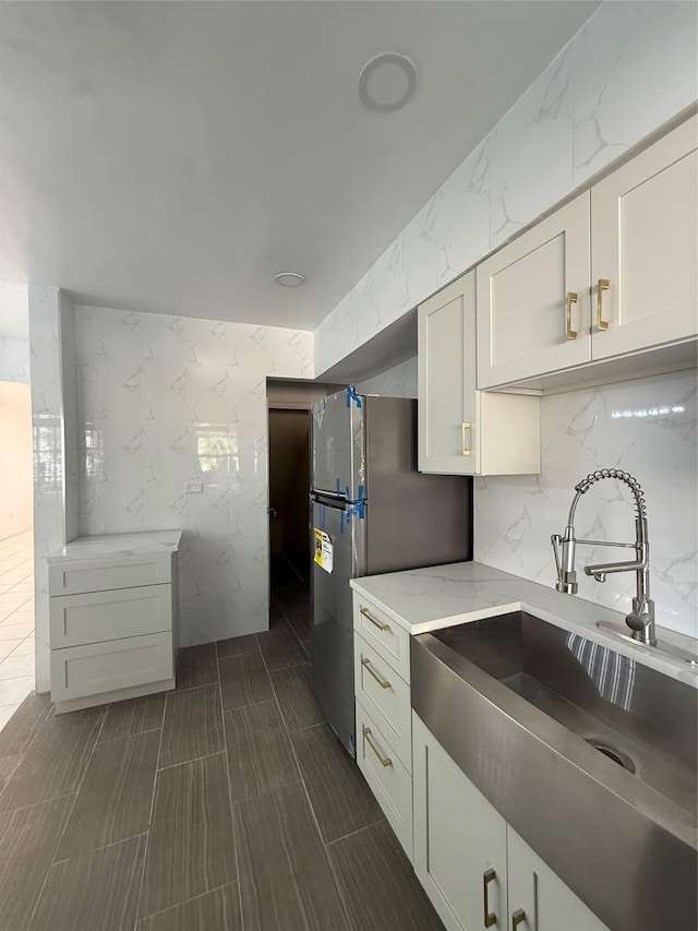 kitchen with a sink, freestanding refrigerator, decorative backsplash, light stone counters, and white cabinetry