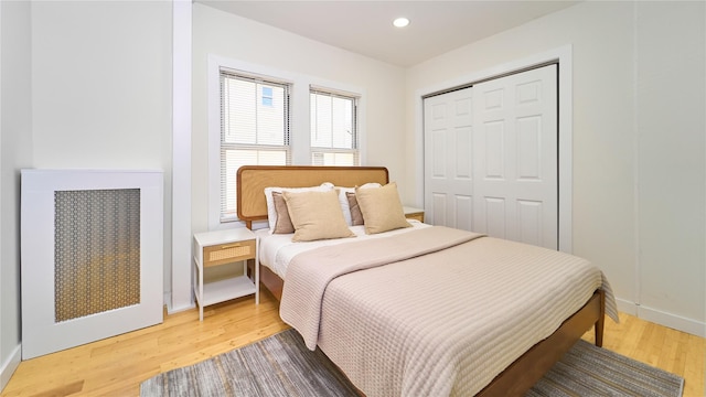 bedroom with light wood-type flooring, radiator, baseboards, and a closet