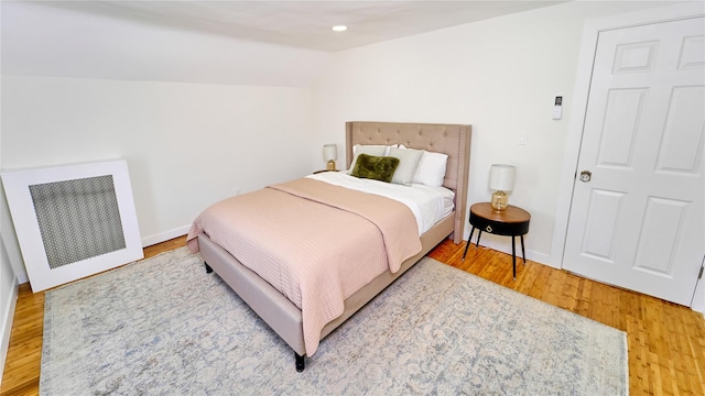 bedroom featuring radiator, baseboards, wood finished floors, and lofted ceiling