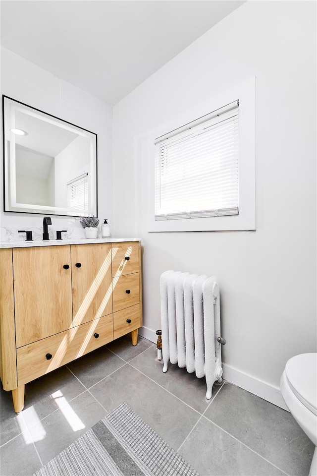 bathroom featuring toilet, baseboards, radiator heating unit, and tile patterned floors