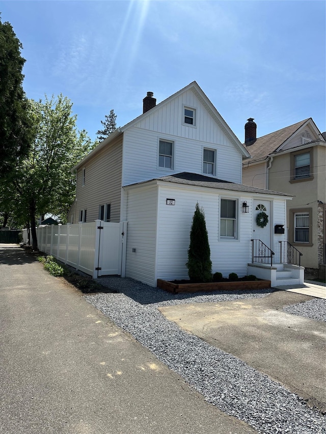 view of front of home featuring board and batten siding, fence, a chimney, and a gate