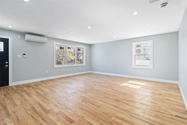 interior space with light wood-style floors, baseboards, a wall unit AC, and recessed lighting