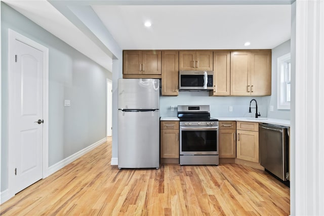 kitchen featuring light countertops, a sink, appliances with stainless steel finishes, light wood-style floors, and recessed lighting